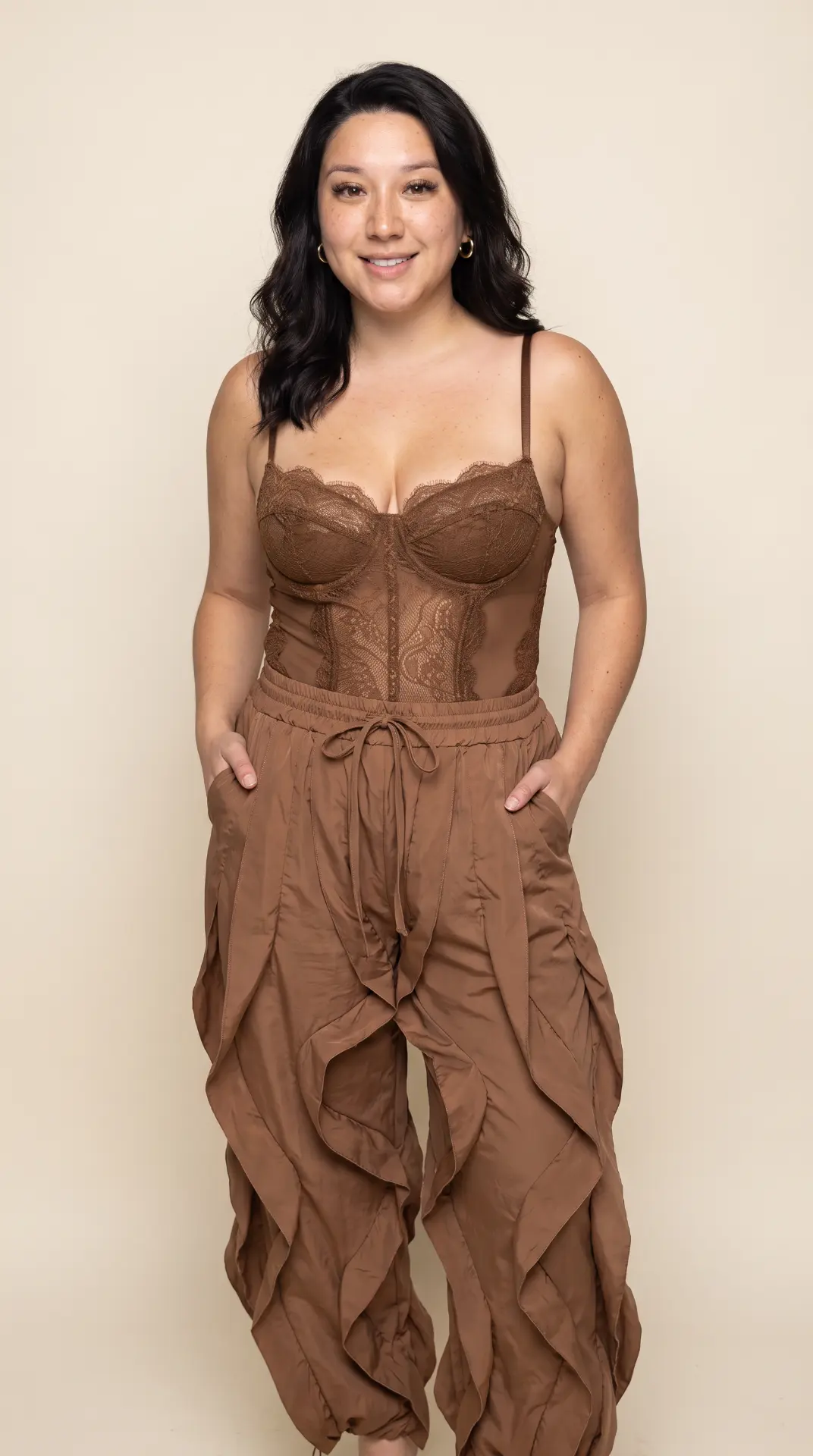 Kayla Bejarano standing in a warm brown lace bodysuit and draped trousers